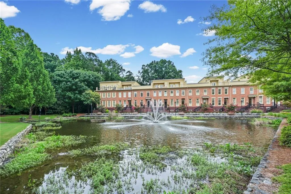 Community pond with a beautiful central fountain, bordered by a paved walkway and mature landscaping
