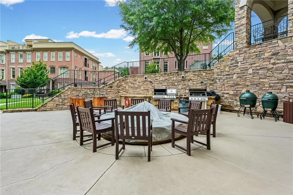 Expansive paved patio with a built-in fire pit, stone accent walls, two built-in grills, and two green egg-style smokers