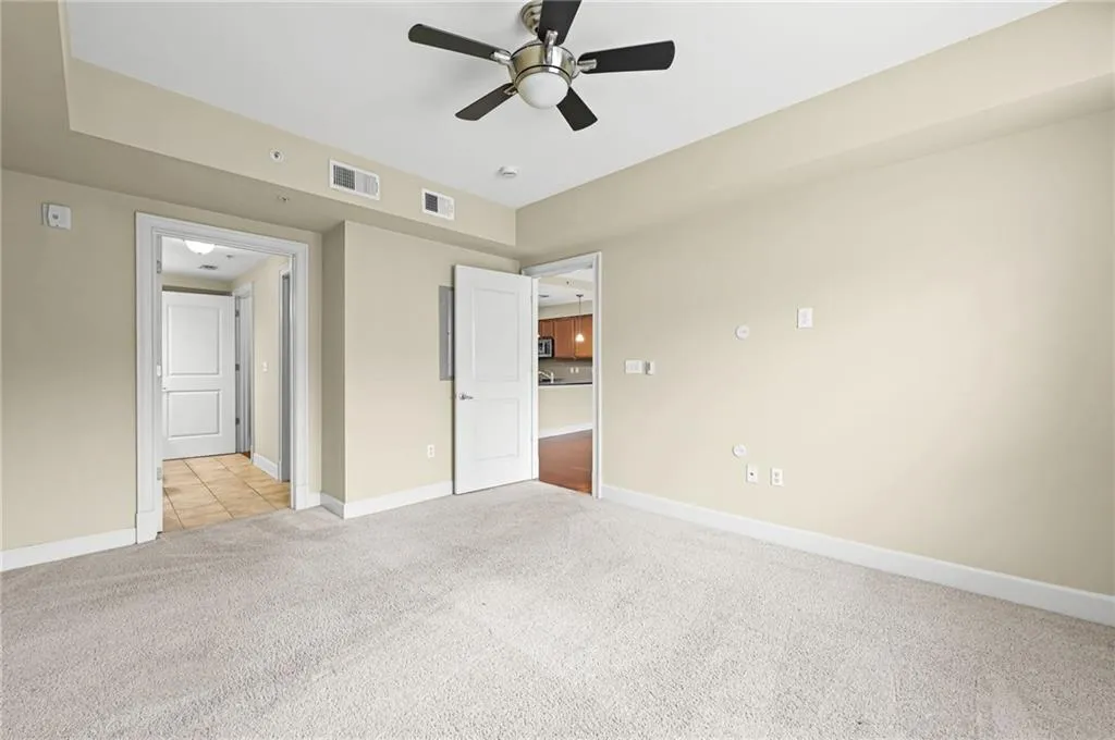 Large primary bedroom with neutral wall tones and neutral colored carpet, adjacent to custom closet system and bathroom.