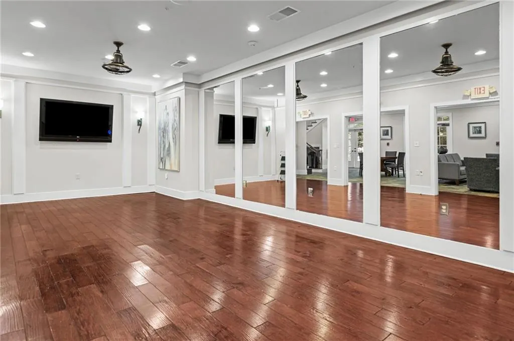 Spacious room featuring rich wood-finish flooring, recessed lighting, and a wall of integrated mirrors located in community clubhouse