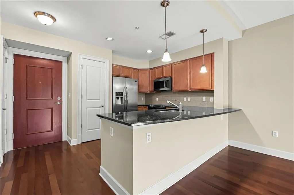 Contemporary kitchen featuring wood-finish flooring, ample cabinetry, stainless steel appliances, a breakfast bar, and pendant lighting