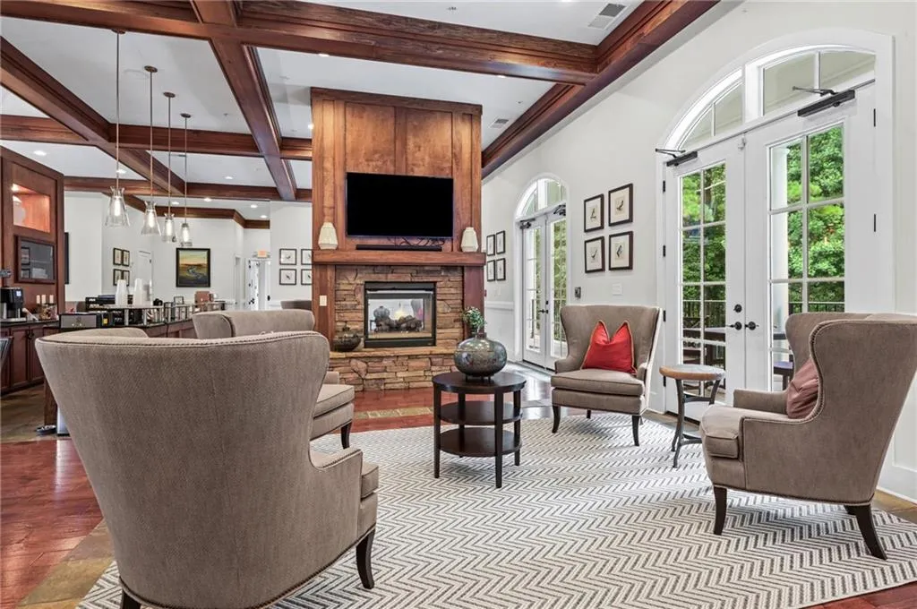 Spacious room featuring a stone fireplace with a wood-paneled surround, coffered ceiling, and multiple arched French doors located in community clubhouse
