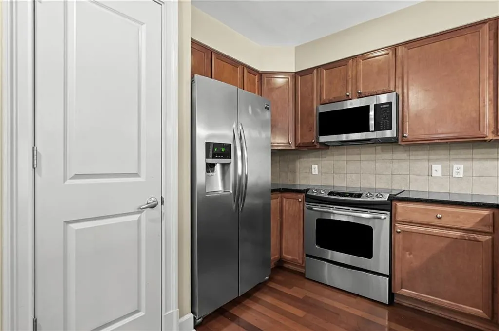 Kitchen featuring wood-finish flooring, dark wood cabinetry, and stainless steel appliances including a side-by-side refrigerator, electric range, and microwave
