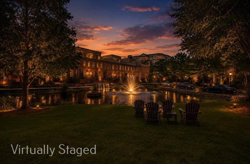 Community pond with a illuminated central fountain, bordered by a paved walkway and mature landscaping