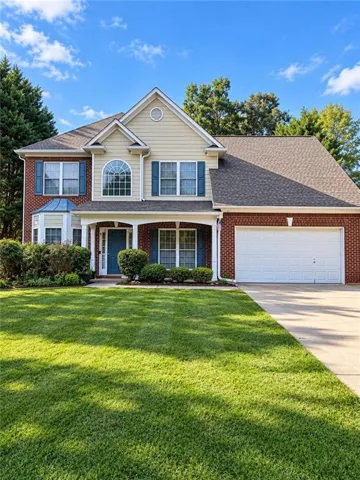 Brick and siding exterior with a covered porch, arched window, attached garage, and landscaped front yard
