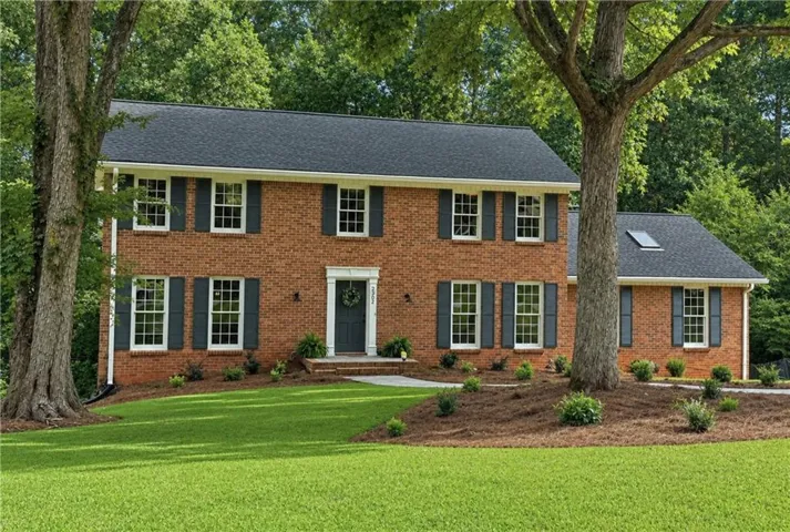 Traditional brick residence featuring a dark shingle roof, white window trim, and dark shutters