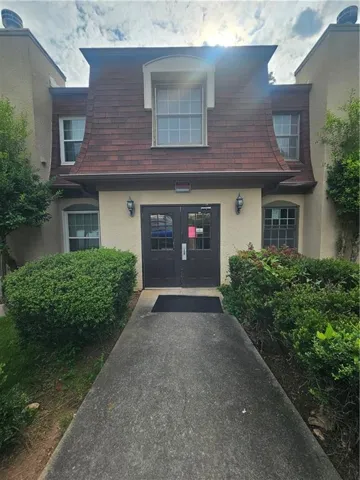 French Colonial exterior featuring a mansard roof with dormer windows, a stucco facade, double entry doors, and a concrete pathway flanked by mature shrubs
