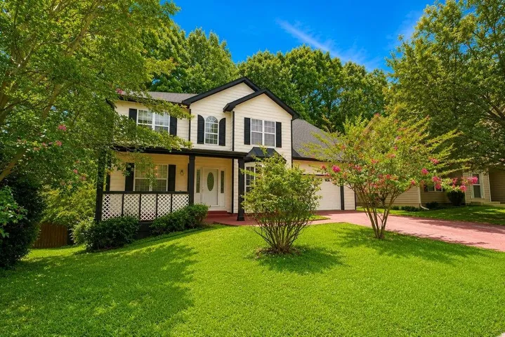 Traditional two-story home featuring a covered front porch with lattice detailing, contrasting dark shutters, and a two-car garage