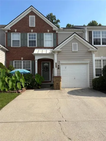 Two-story townhome featuring a brick facade with shuttered windows and an attached garage