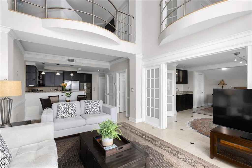 Two-story living area featuring a kitchen bar, curved balcony with metal railings, and double French doors opening to a wet bar with a stone countertop