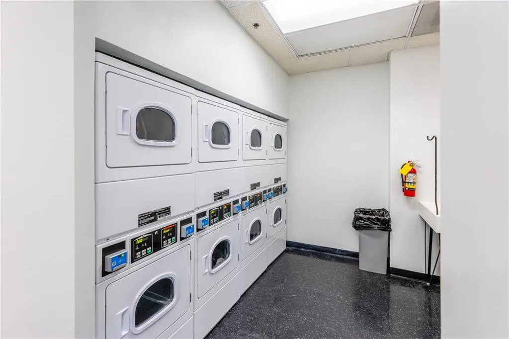 Laundry facility with multiple stacked washer and dryer units, white walls, and dark speckled flooring
