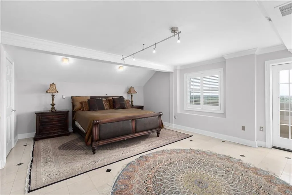 Spacious room featuring light-toned flooring with dark accent tiles, a large window with white louvered shutters, and a white paneled door