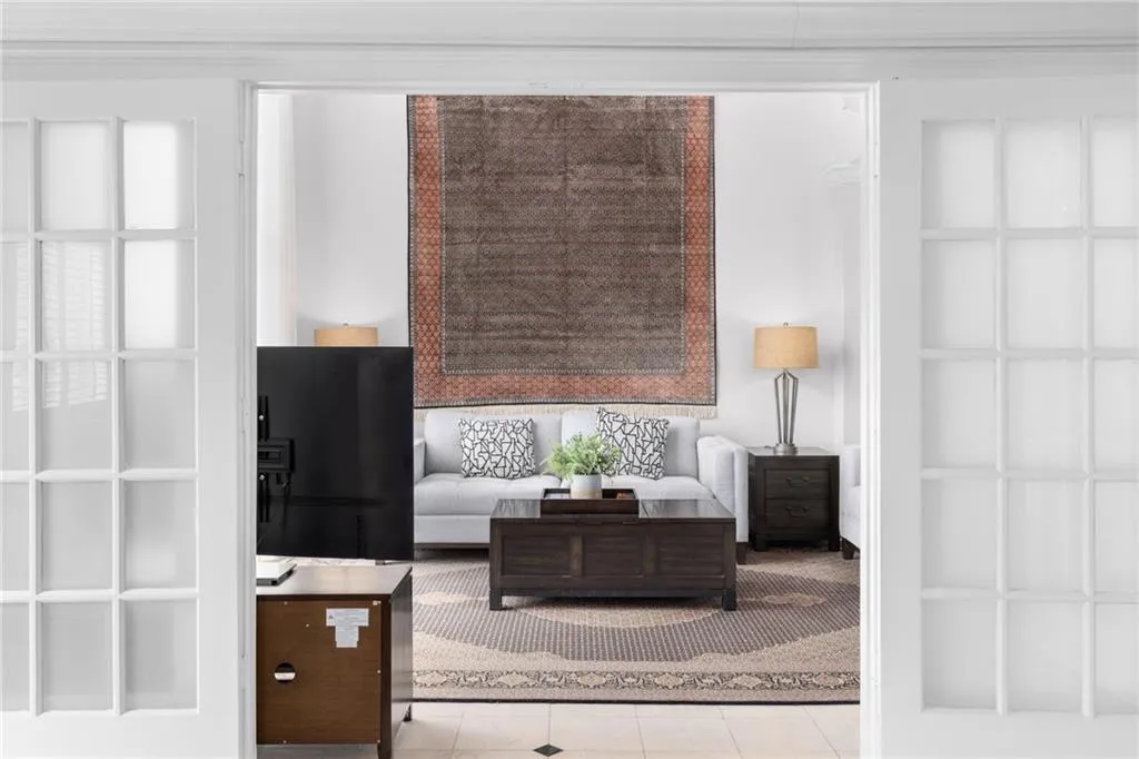 Interior space featuring white French doors with glass panes opening into a living area with a light-colored sofa, dark wood-finish coffee table, and area rug