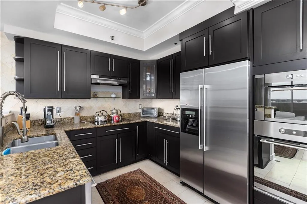 Kitchen featuring dark shaker-style cabinetry, stainless steel appliances, granite countertops, and a tile backsplash