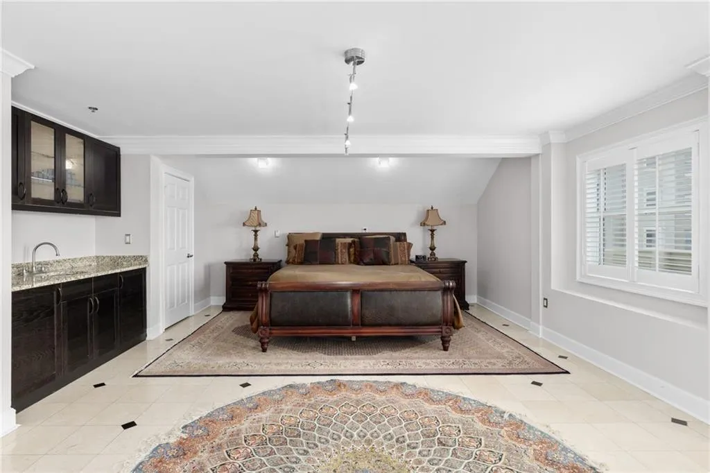 Spacious room featuring light-toned tile flooring with dark accent squares, a built-in wet bar with dark cabinetry and granite countertop, crisp white window shutters, a white paneled door, and recessed lighting
