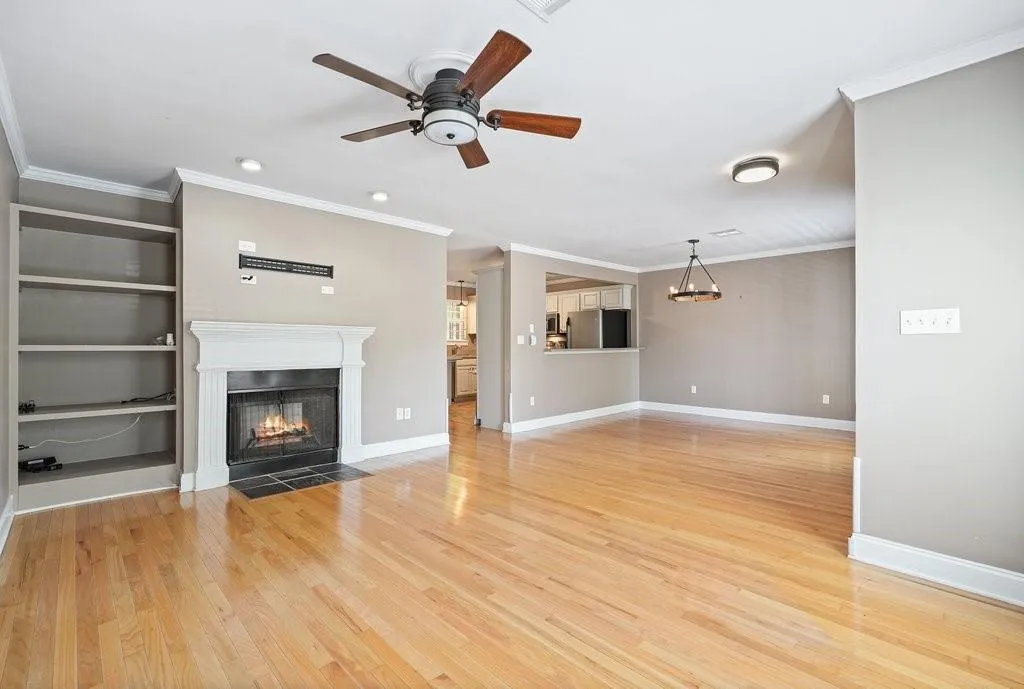 Unfurnished living room with light hardwood / wood-style floors, crown molding, ceiling fan, and a fireplace