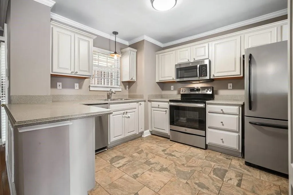 Kitchen with hanging light fixtures, crown molding, white cabinetry, stainless steel appliances, and light tile floors