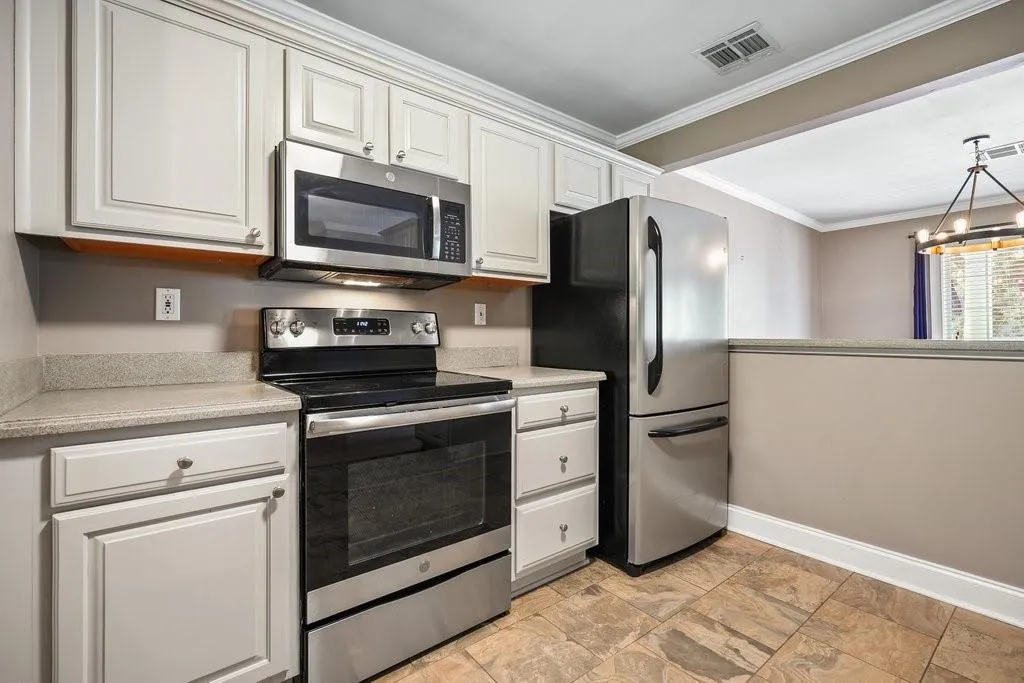 Kitchen featuring hanging light fixtures, stainless steel appliances, light tile flooring, a chandelier, and ornamental molding