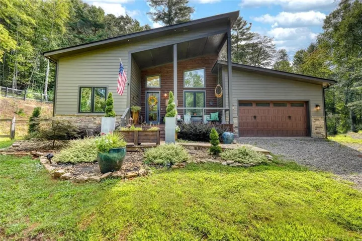 Contemporary exterior with a covered porch, wood-finish garage door, stone accents, and sloped roofline