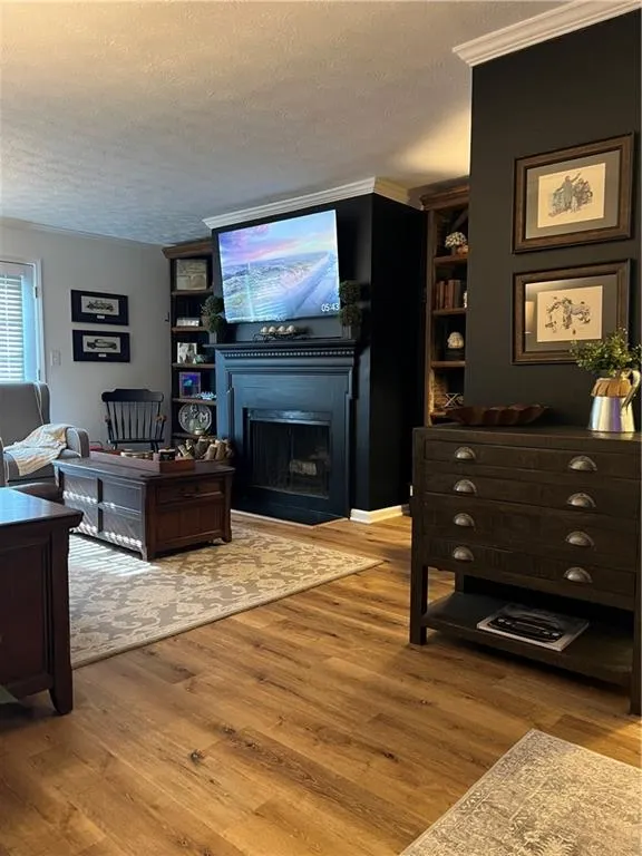 Living room featuring a textured ceiling, a fireplace, light wood-type flooring, and ornamental molding