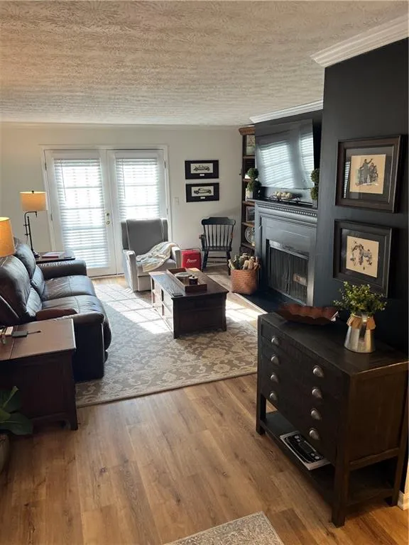 Living area featuring a fireplace, light wood-type flooring, a textured ceiling, and ornamental molding