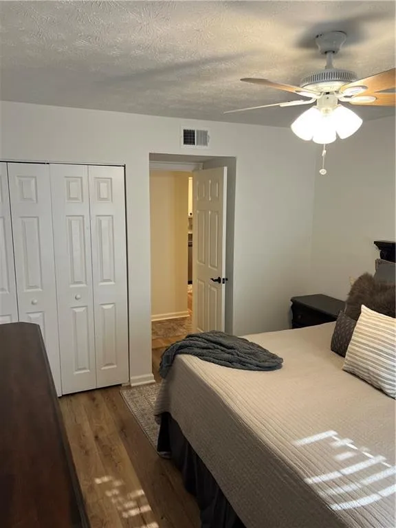 Bedroom with dark wood-style floors, a textured ceiling, a closet, and a ceiling fan