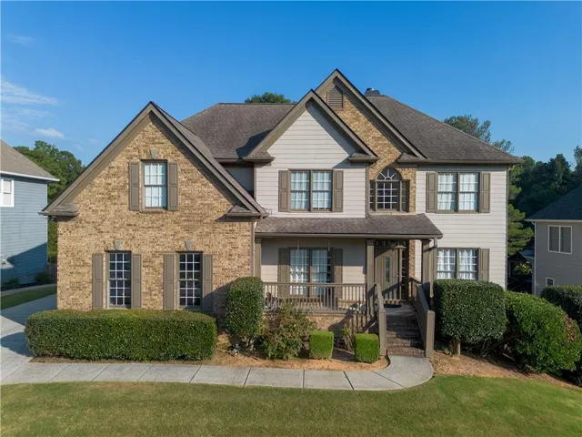 Two-story residence featuring a brick and siding exterior, multiple gables, an arched window, a covered front porch, and mature landscaping