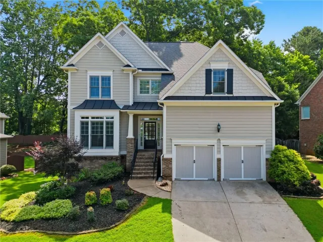 Two-story residence featuring light gray siding with stone accents, a two-car garage, and a concrete driveway