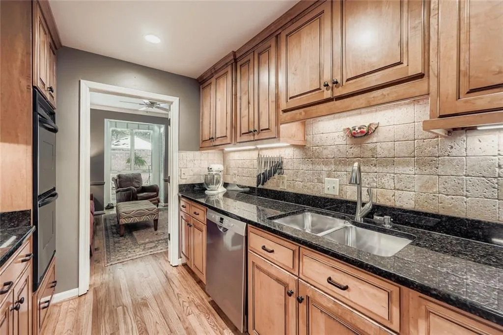 Kitchen featuring backsplash, light wood finished floors, dark stone countertops, dishwasher, and double wall oven