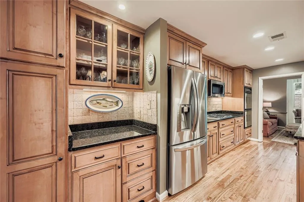 Kitchen featuring glass insert cabinets, stainless steel appliances, backsplash, light wood-style floors, and dark stone countertops