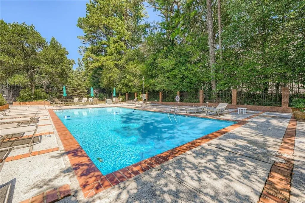 Community pool with a patio and view of wooded area