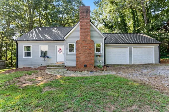 Exterior featuring horizontal siding, a red brick chimney, a dark metal roof, and a two-car garage