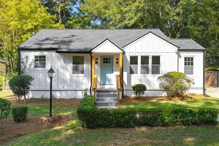 White exterior with vertical and horizontal siding, light blue entry door, dark gray shingles, and exterior lighting fixtures