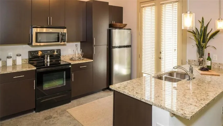 Kitchen featuring stainless steel appliances, a peninsula, light stone countertops, and hanging light fixtures