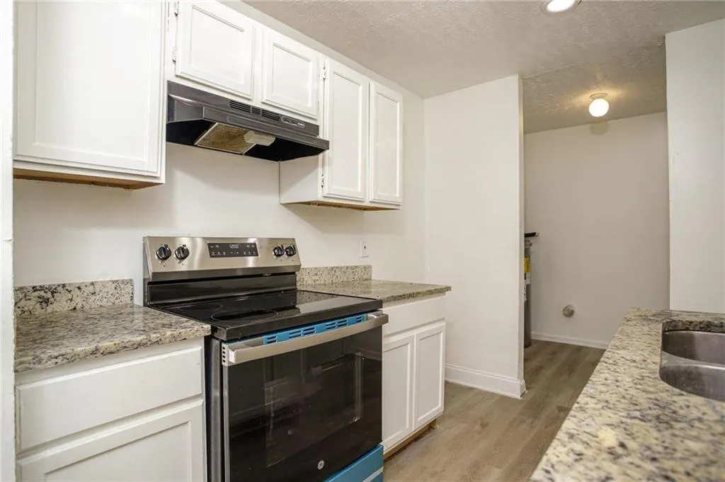 Kitchen featuring under cabinet range hood, stainless steel electric stove, white cabinetry, light wood-style flooring, and a textured ceiling