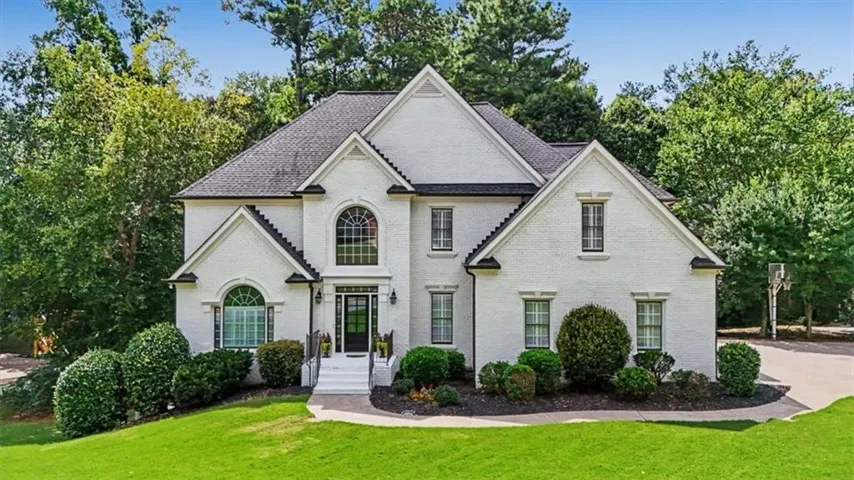 White brick exterior, gabled roofline, arched windows, prominent entry, and established landscaping