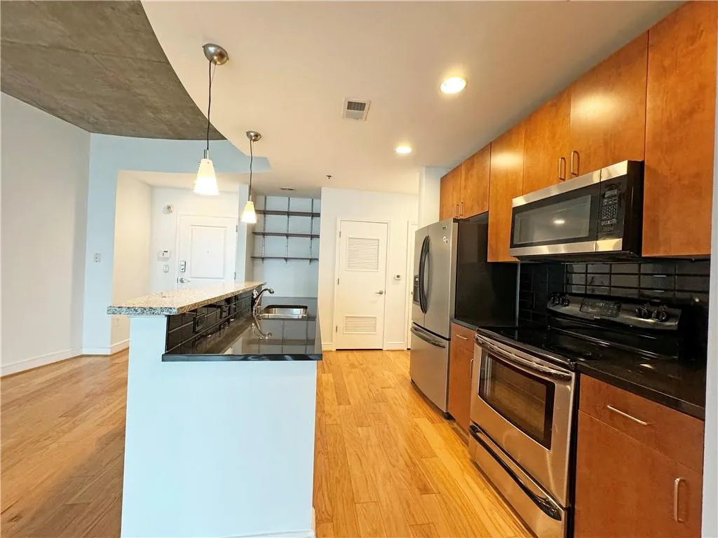 Kitchen with appliances with stainless steel finishes, hanging light fixtures, a kitchen island with sink, and light wood finished floors