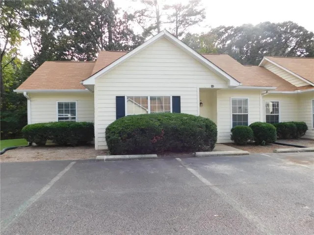 Light-colored siding exterior with a brown shingle roof, dark shutters, and a built-in outdoor light fixture