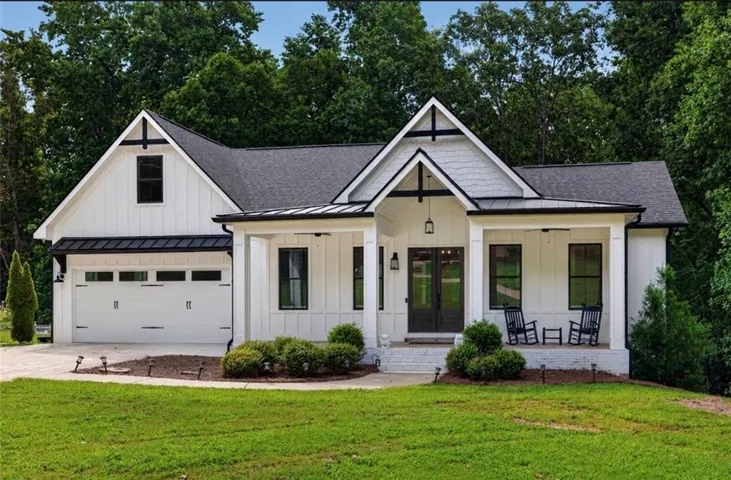 Modern farmhouse exterior featuring white board and batten siding, black trim accents, a prominent covered front porch, and a two-car garage with carriage-style doors