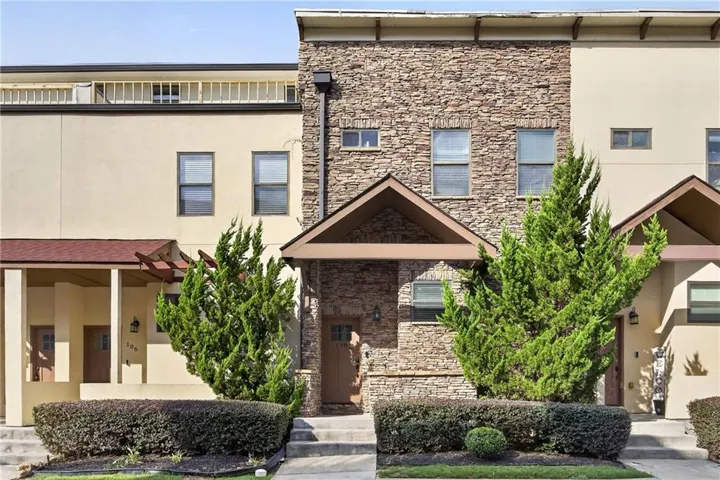 Contemporary brick and stone facade featuring a gabled entryway with dark wood detailing, multiple window openings, and manicured evergreen landscaping