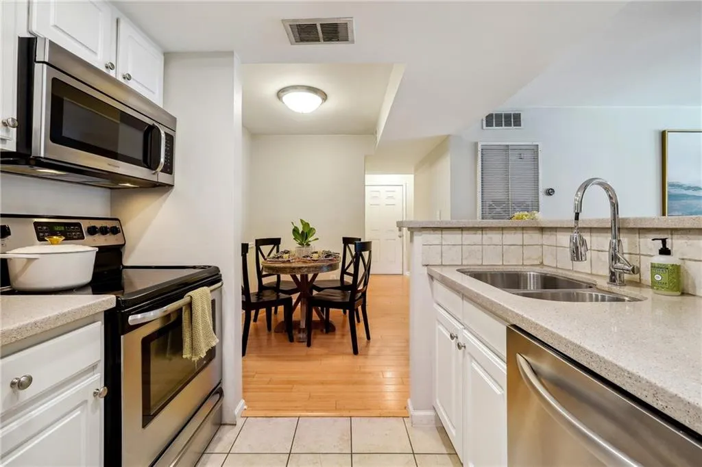 Kitchen with appliances with stainless steel finishes, white cabinets, sink, light hardwood / wood-style floors, and light stone countertops