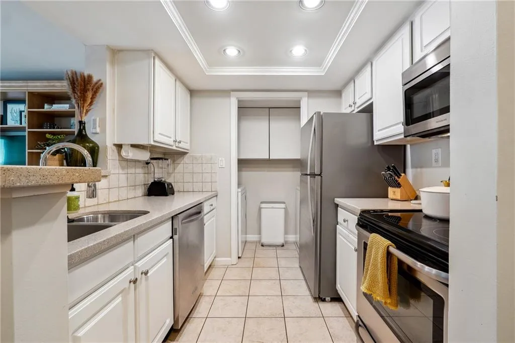 Kitchen featuring white cabinetry, light tile patterned floors, backsplash, a tray ceiling, and stainless steel appliances