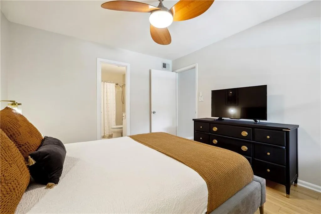 Bedroom with ensuite bathroom, light wood-type flooring, and ceiling fan