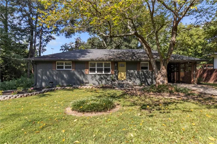 Brick exterior, mature trees, landscaped front yard, wood-tone shutters, and a covered carport