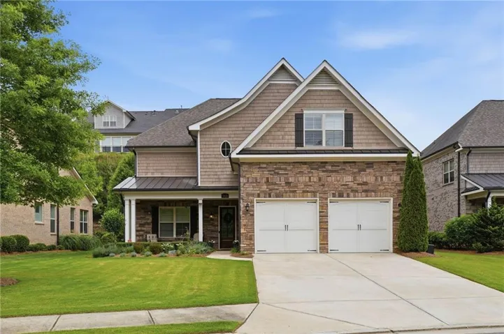 Brick and shake exterior with a covered porch, two-car garage, and mature landscaping