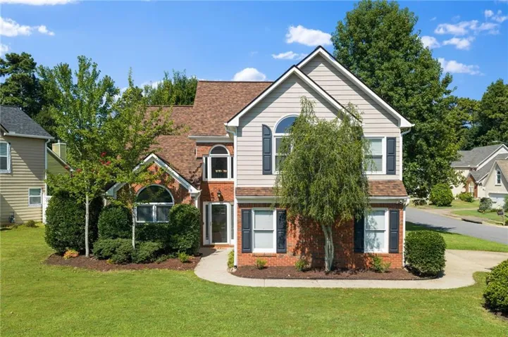 Two-story residence featuring brick and siding exterior, arched window details, dark shutters, and an inviting curved front walkway