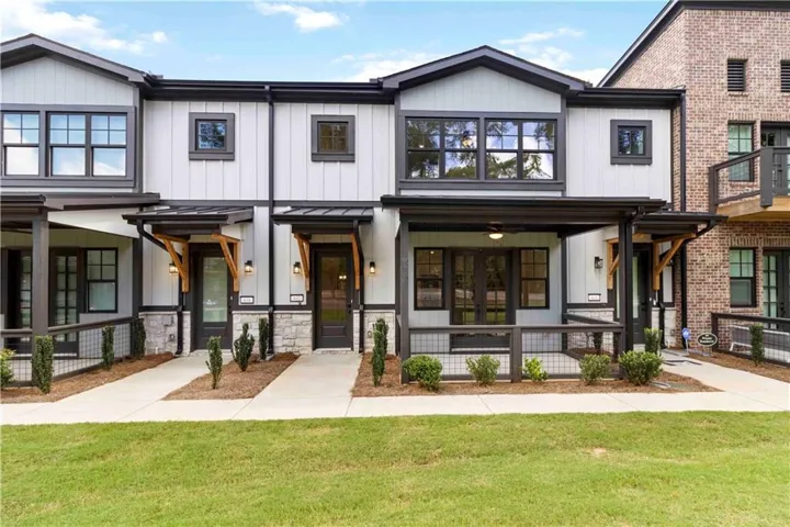 Modern townhome exterior featuring light-toned siding, dark-trimmed windows, and stone accents