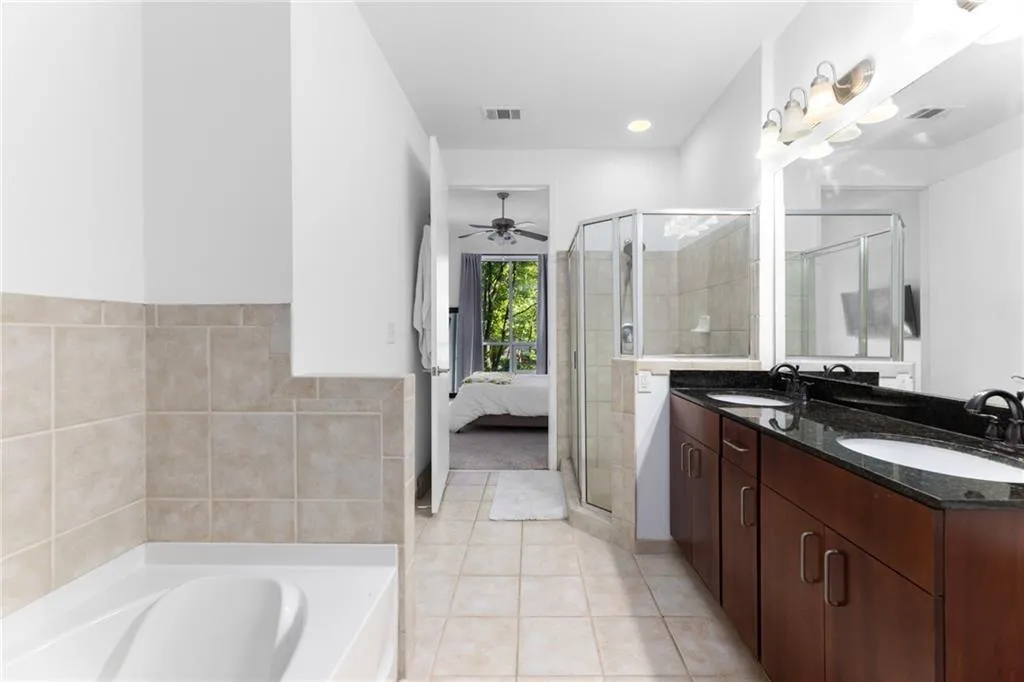 Ensuite bathroom with double vanity, tile patterned floors, ceiling fan, a garden tub, and a shower stall