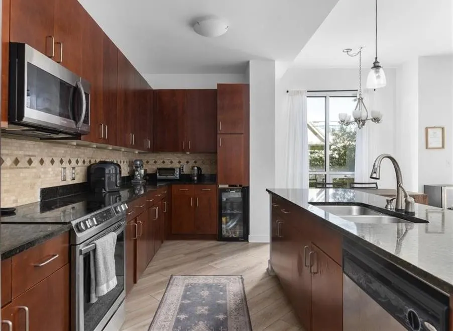 Kitchen featuring stainless steel appliances, decorative backsplash, light wood finished floors, dark stone countertops, and pendant lighting