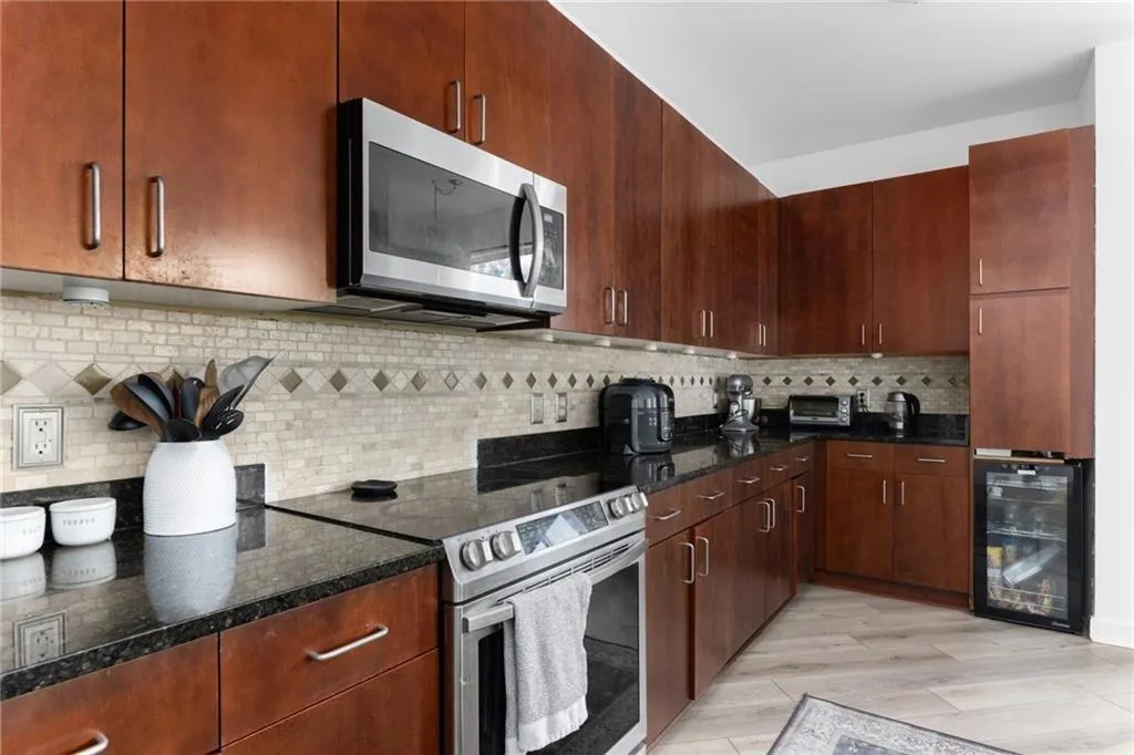 Kitchen featuring appliances with stainless steel finishes, beverage cooler, dark stone counters, and decorative backsplash
